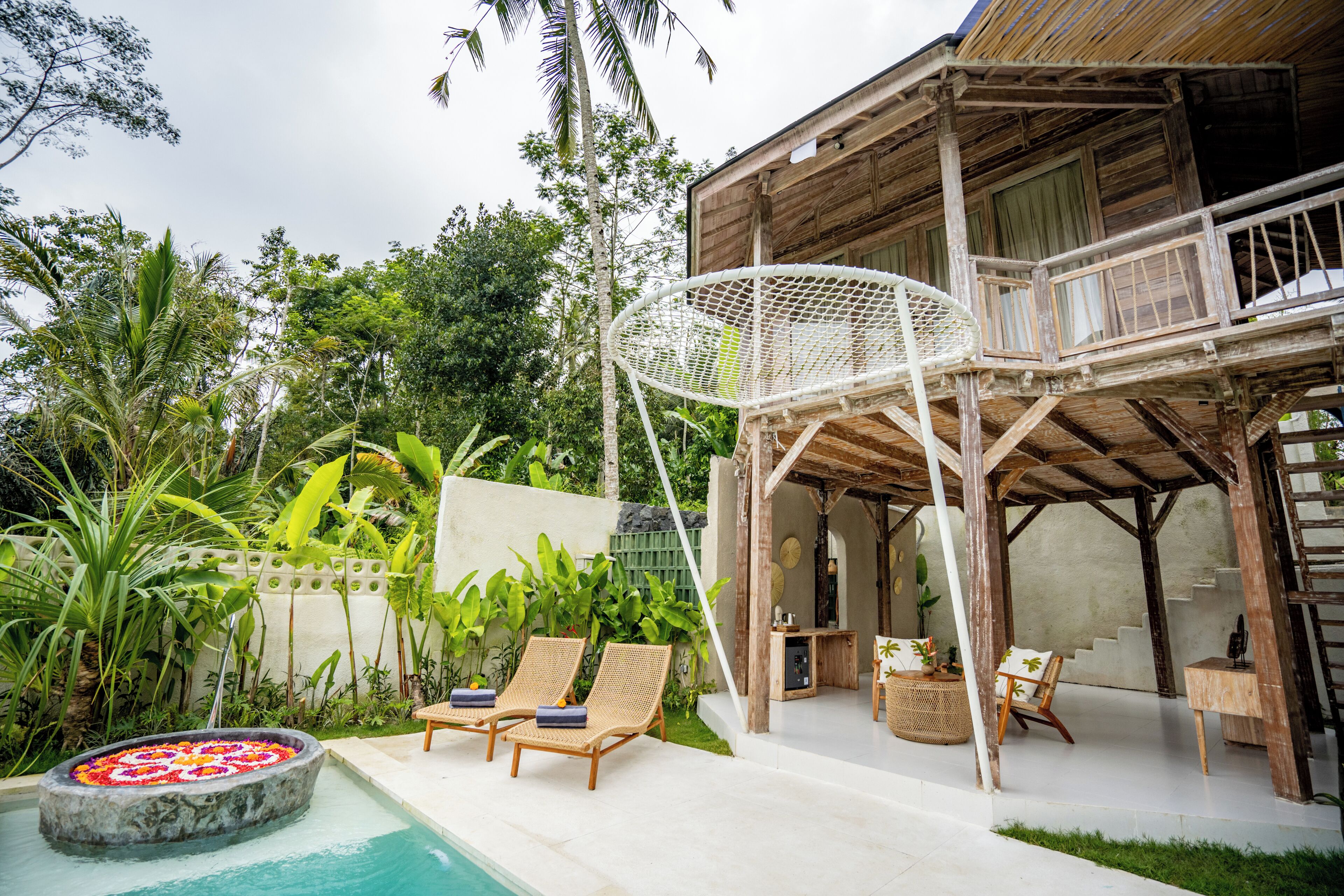 A wooden house with a pool, lounge chairs, and a hanging chair.