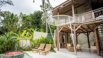 A wooden house with a pool, lounge chairs, and a hanging chair.