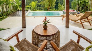 A covered outdoor area with a pool, wicker furniture, and lush greenery in the background. - Moonlit Jungle (Tampaksiring)