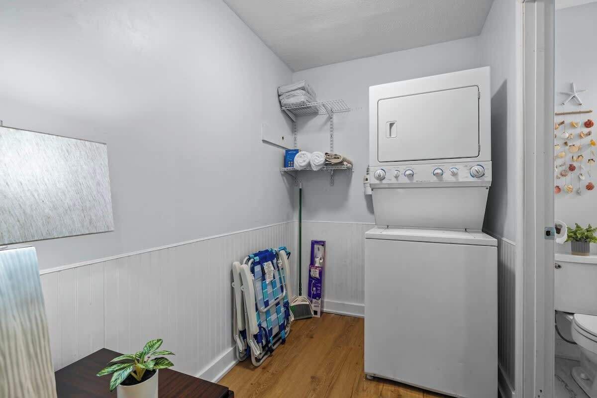 Ett kompakt tvättrum med en tvättmaskin och torktumlare placerade ovanpå varandra, ett torkställ och en hylla med handdukar och hygienartiklar.