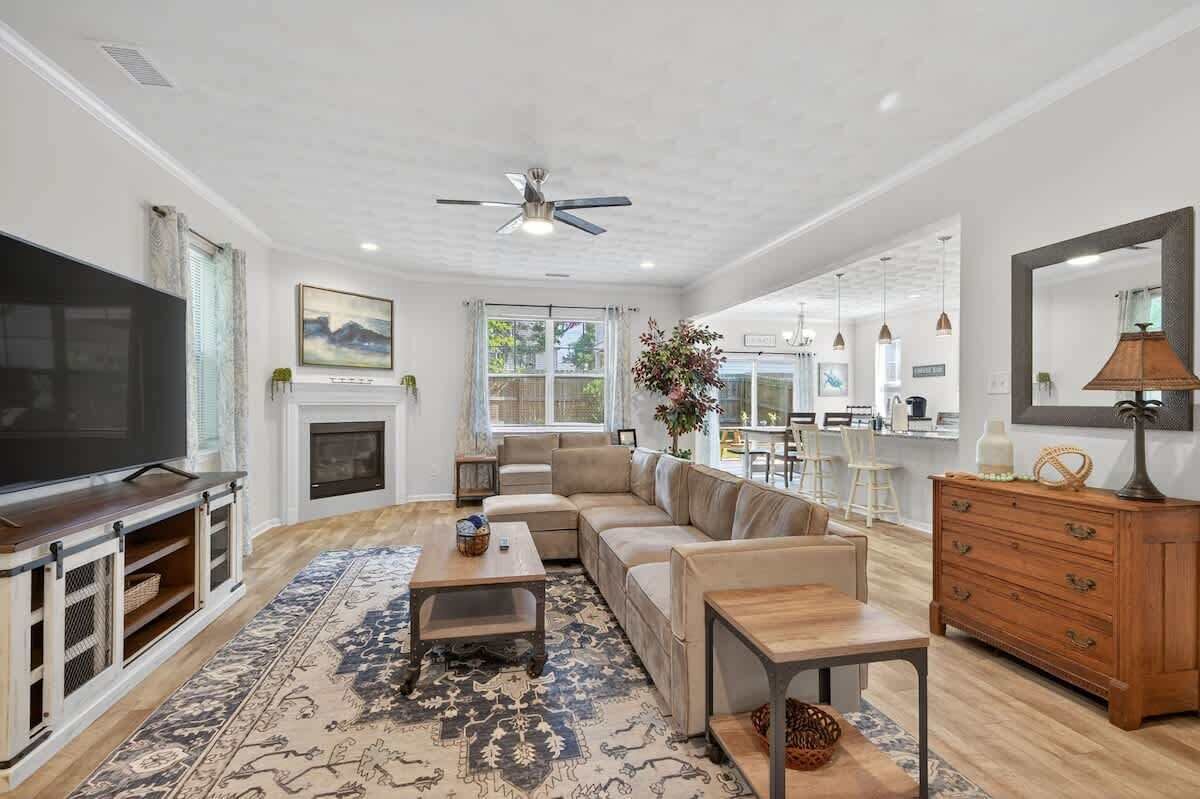 A spacious living room with a large sectional sofa, a flat-screen TV, a fireplace, and a dining area in the background.