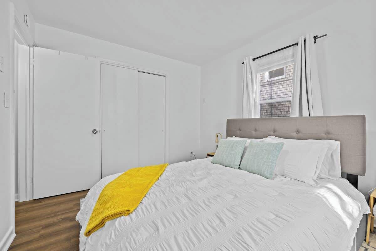 Un dormitorio con cama, una colcha amarilla y una ventana con cortinas.