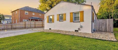 A two-story house with a white exterior and wooden shutters, a fenced yard, and a neighboring brick house.