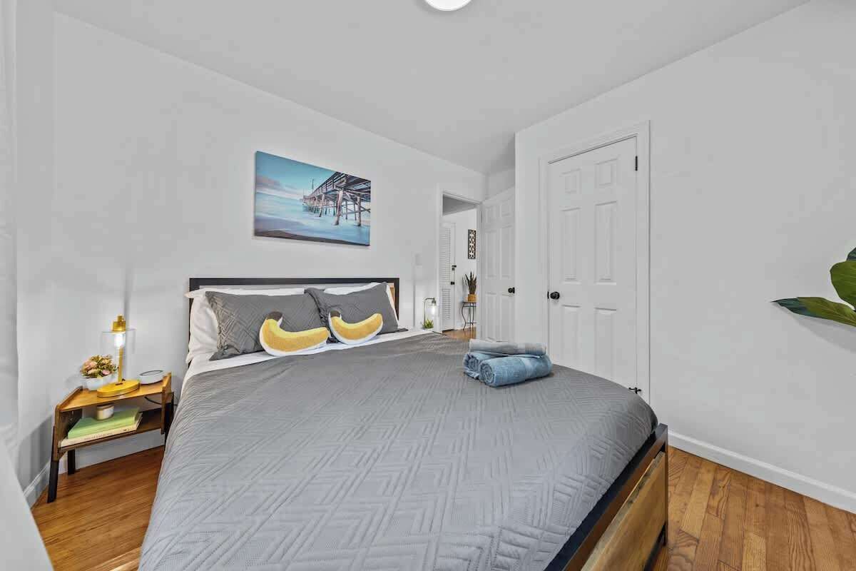 Ein Schlafzimmer mit Bett, Nachttisch, Lampe, einem Gemälde und einer Tür.