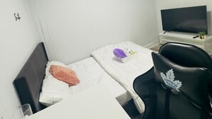 Ein kleiner, ordentlich eingerichteter Raum mit einem Bett, einem Schreibtisch, einem Stuhl und einem Fernseher.
