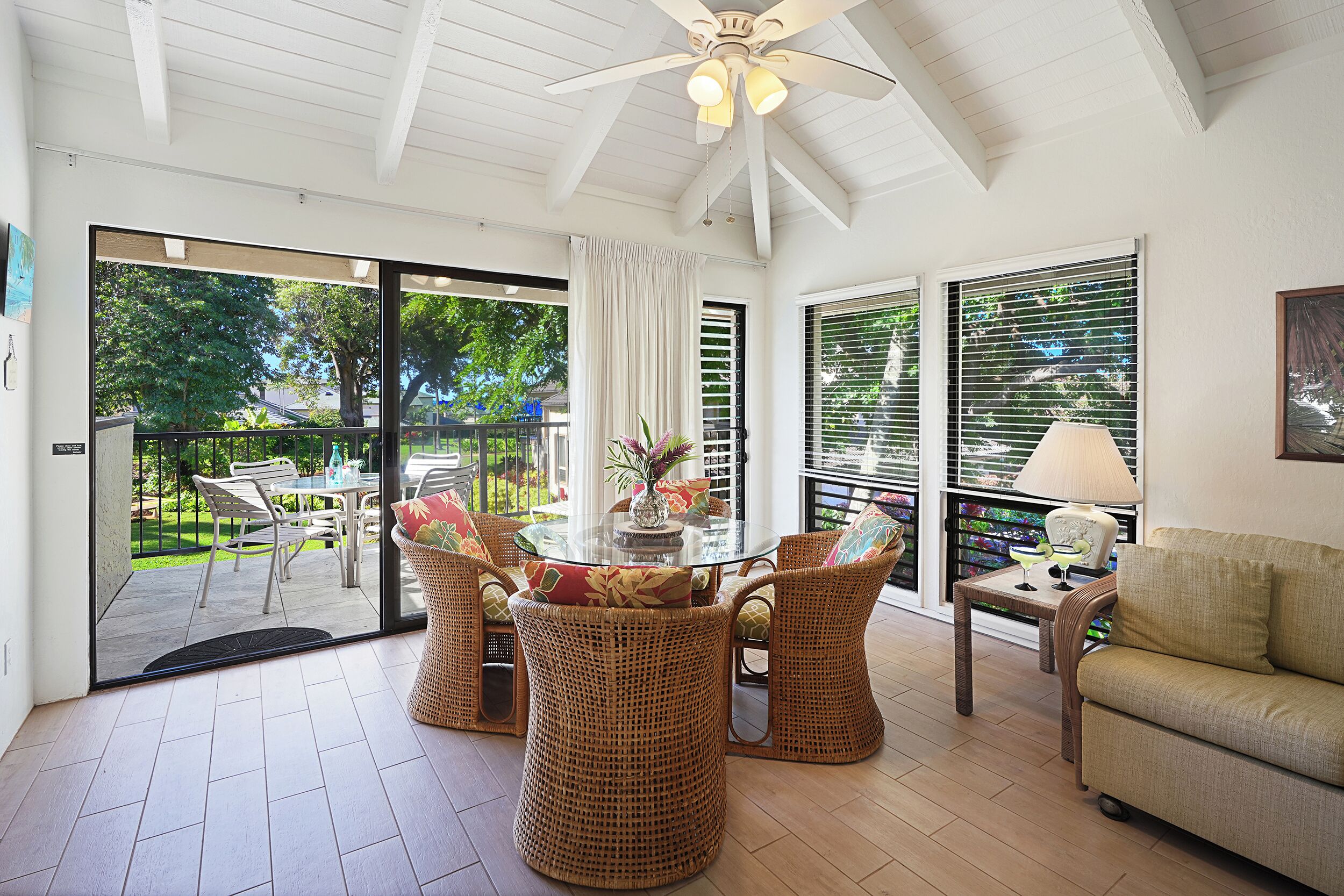 A spacious room with a glass door leading to a balcony, wicker furniture, a round table, and a ceiling fan.