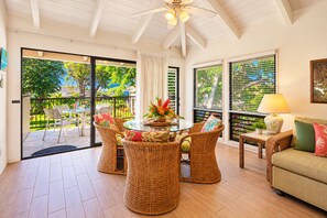 A room with a dining table surrounded by wicker chairs, a sofa, and a ceiling fan. - Kahala 723 “Apana O Lani” – 2 Lanais, King Bed, Island Serenity (Koloa)