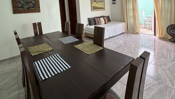A dining area with a large table, chairs, and a sofa in the background. - Beach house in Buzios for up to 8 people. (Armação dos Búzios)