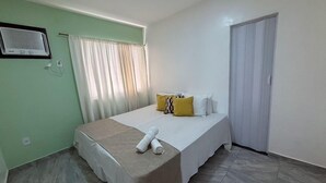 A hotel room with a bed, a window with curtains, a door, and a wall-mounted air conditioning unit. - Beach house in Buzios for up to 8 people. (Armação dos Búzios)