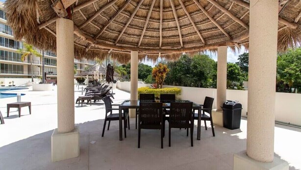 Un patio exterior con techo de paja, sillones de descanso y una piscina.