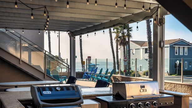 Eine Terrasse im Freien mit einem Weber-Grill, einer Sitzgelegenheit und Blick auf das Meer und Häuser.