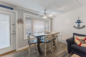 A dining area with a table and chairs, a ceiling fan, and a sign above the door. - Oceanview 1 BR Condo with Pool Access & Central AC (Wildwood Crest)