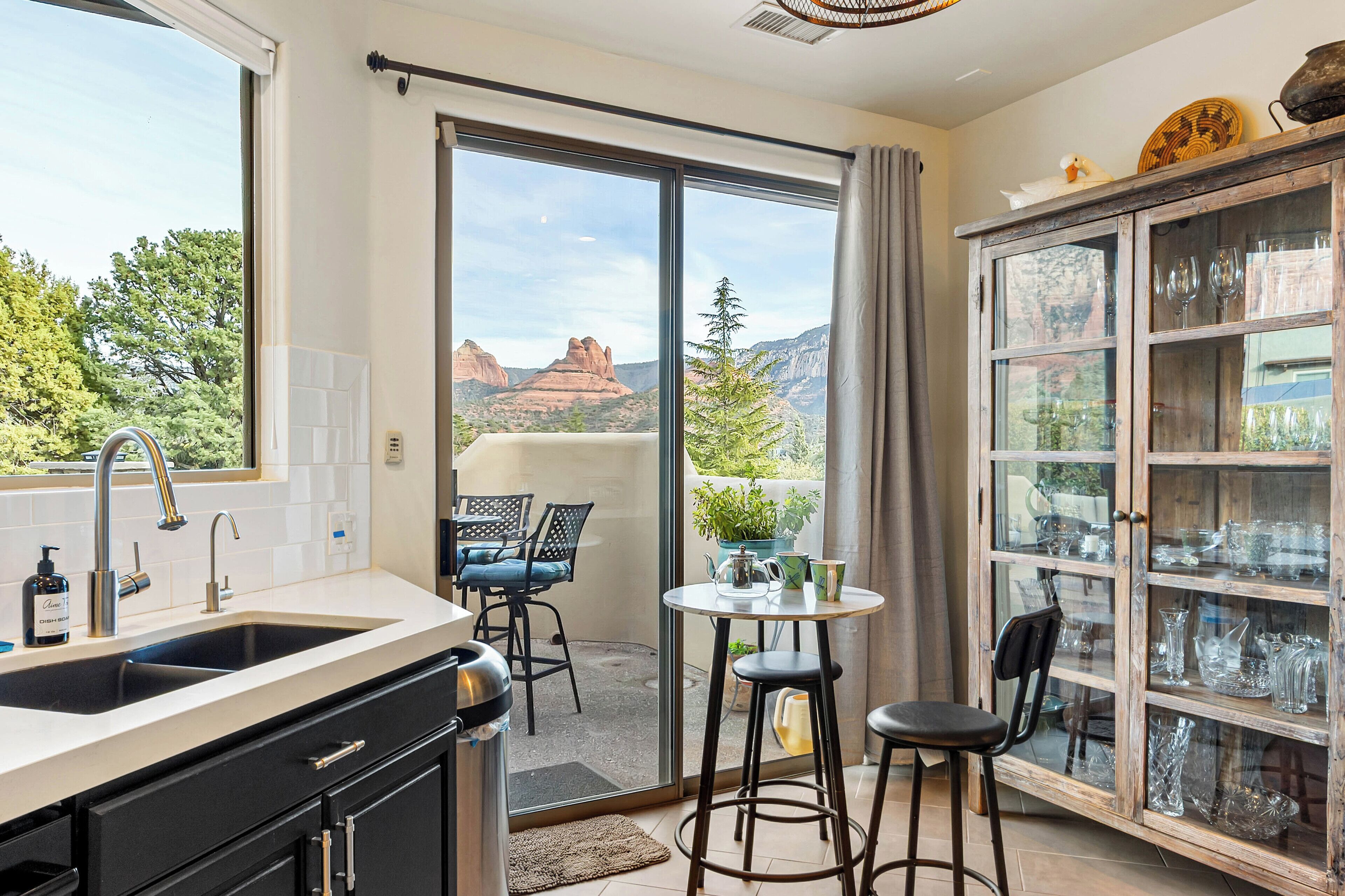 Une cuisine équipée d’un évier, un coin repas avec une table et des chaises, et un meuble vitré contenant de la verrerie.