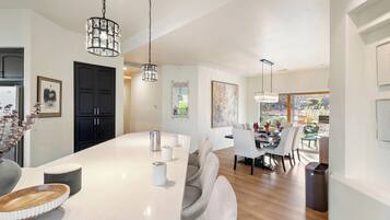 Une cuisine moderne dotée d’un grand îlot central, de luminaires suspendus et d’un coin repas avec des chaises et une table.