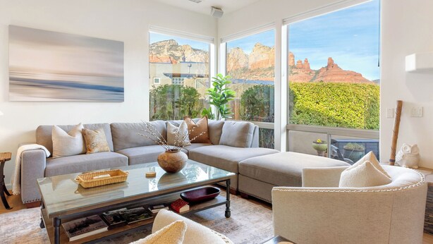 A modern living room with a sectional sofa, a glass coffee table, and a view of red rock formations. - Experience luxury at Sedona Willow Villa—spacious 3BR home with stunning Red Rock views! (Sedona)