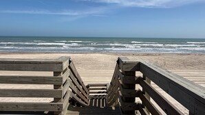 Une promenade en bois menant à une plage, avec des vagues en arrière-plan.
