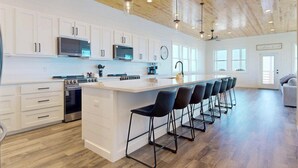 Une cuisine moderne avec des meubles blancs, un îlot central doté de tabourets, un four à micro-ondes et une cuisinière.