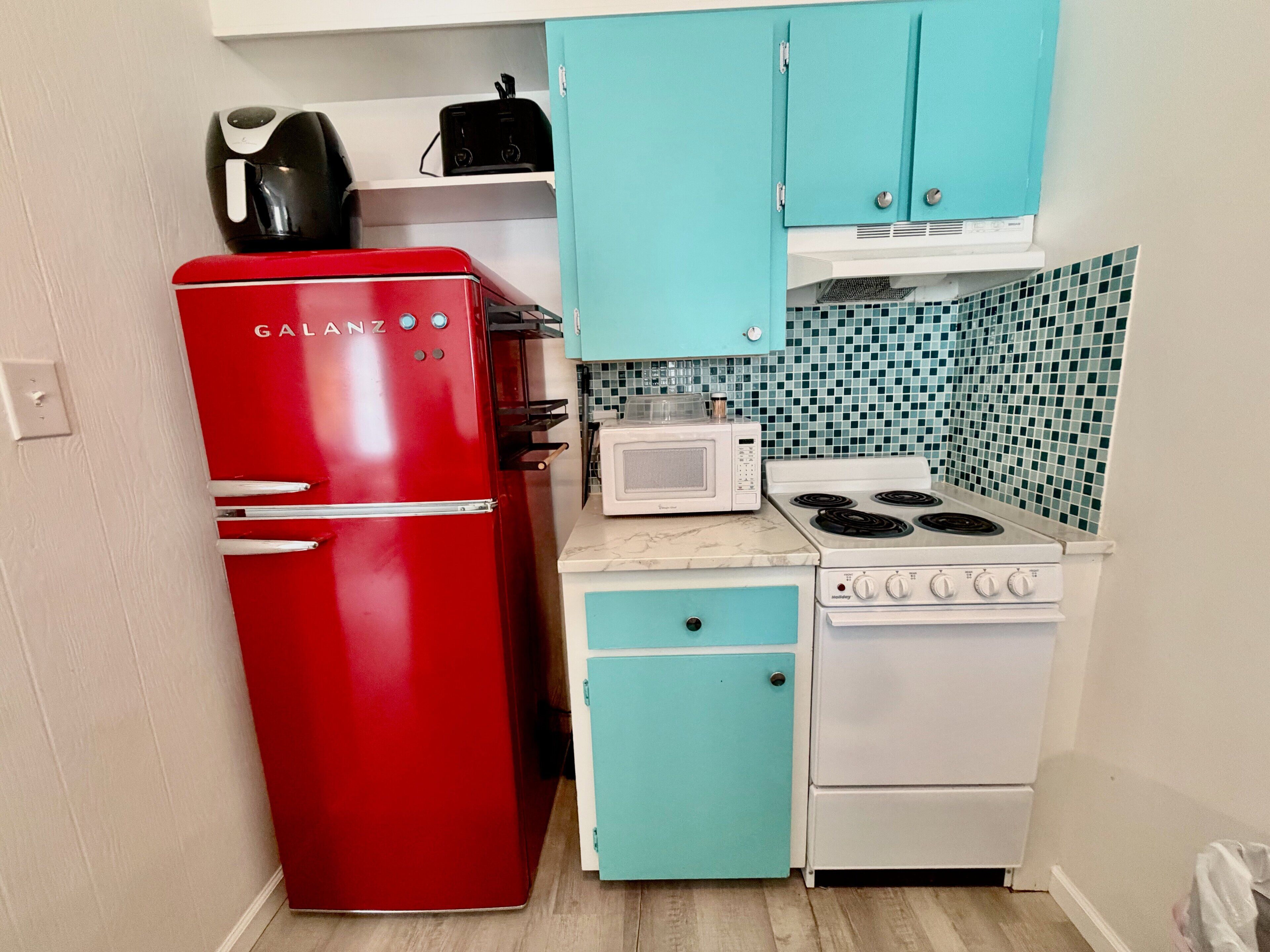 Een compacte keuken met een rode koelkast, een witte kookplaat, een magnetron en turquoise kastjes.