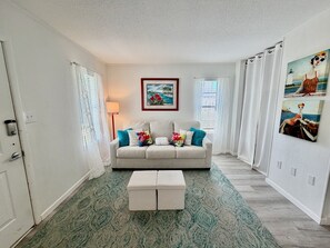 A living room with a sofa, a coffee table, a painting, and a window with curtains.