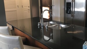 Ett modernt kök med ett kylskåp i rostfritt stål, en inbyggd ugn, en dubbel diskho och två barstolar.
