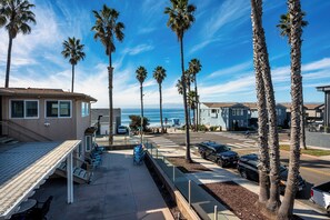 A coastal hotel with a patio area, palm trees, and a view of the ocean. - Steps to the Shore – Top Floor 3BR Ocean View -  #4 (Oceanside)