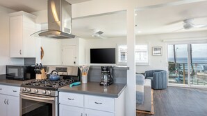 Een moderne keuken met een gasfornuis, magnetron en koffiezetapparaat. Er is een groot raam met uitzicht op de oceaan.