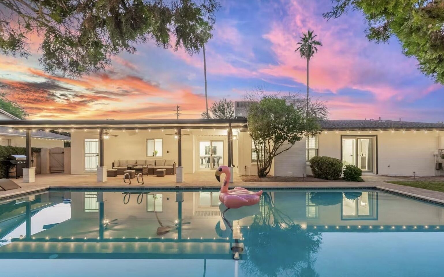 Una piscina con un flotador de flamenco rosa, un patio techado y una casa con techo plano y ventanas amplias.