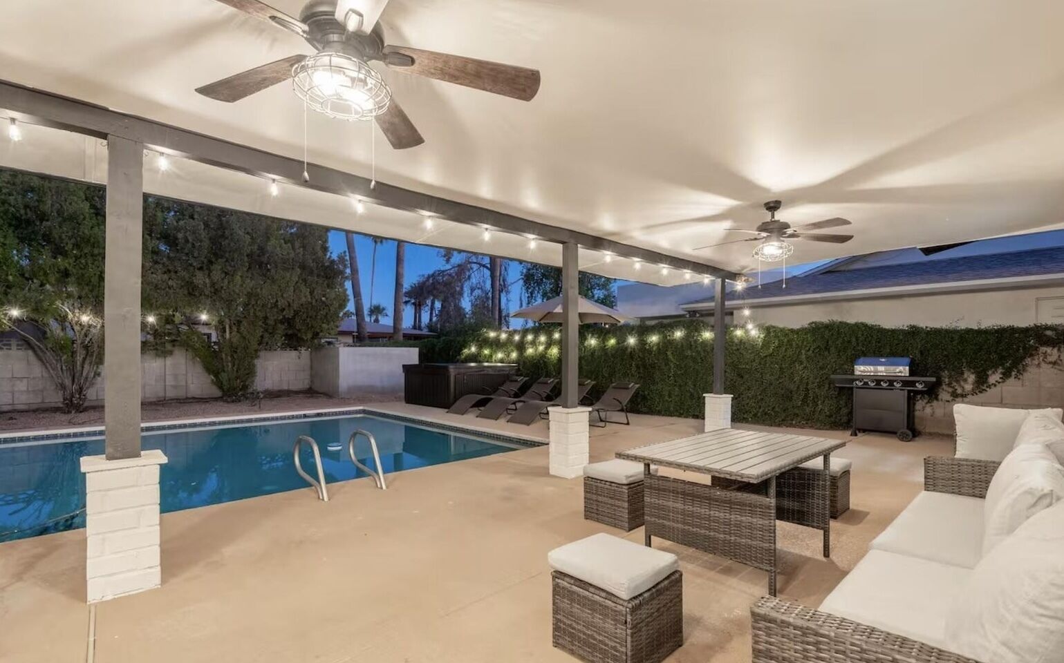 Um pátio externo com piscina, espreguiçadeiras, mesa e ventiladores de teto.