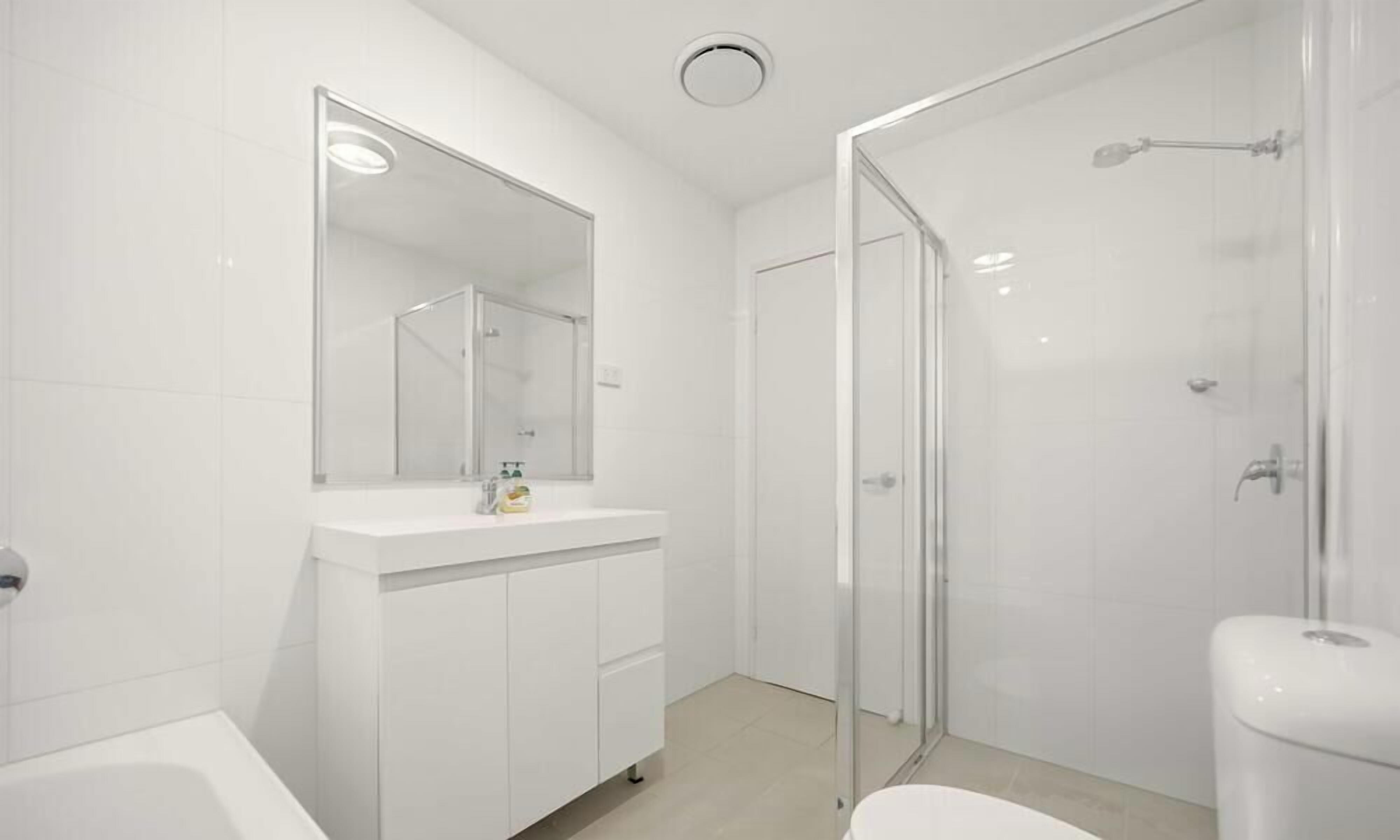 Une salle de bain moderne avec une douche à parois de verre, un lavabo blanc avec un miroir et des toilettes.