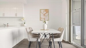 Eine moderne Küche mit weißen Schränken, einem weißen Esstisch mit vier Stühlen, einer Vase mit Blumen und einem gerahmten abstrakten Gemälde an der Wand.
