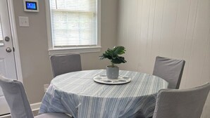 A round dining table with a striped tablecloth, surrounded by four grey upholstered chairs. A potted plant is placed on the table's center. - Comfortable 3BR Home Near Fort Liberty & Medical Center (Fayetteville)