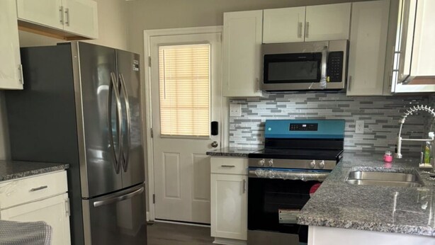 A modern kitchen with stainless steel appliances, white cabinetry, and a tiled backsplash. - Comfortable 3BR Home Near Fort Liberty & Medical Center (Fayetteville)