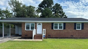 A single-story brick house with a front porch, a white door, and a small set of steps leading to the entrance. - Comfortable 3BR Home Near Fort Liberty & Medical Center (Fayetteville)