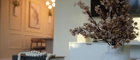 A reception desk with a vase of dried flowers, a white beaded prayer chain, and a stack of luxury brand books.