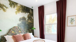 A bedroom with a large bed, a ceiling fan, a window with curtains, and a wall mural. - Historic 2-bedroom house close to beltline in Cabbagetown, Atlanta (Atlanta)