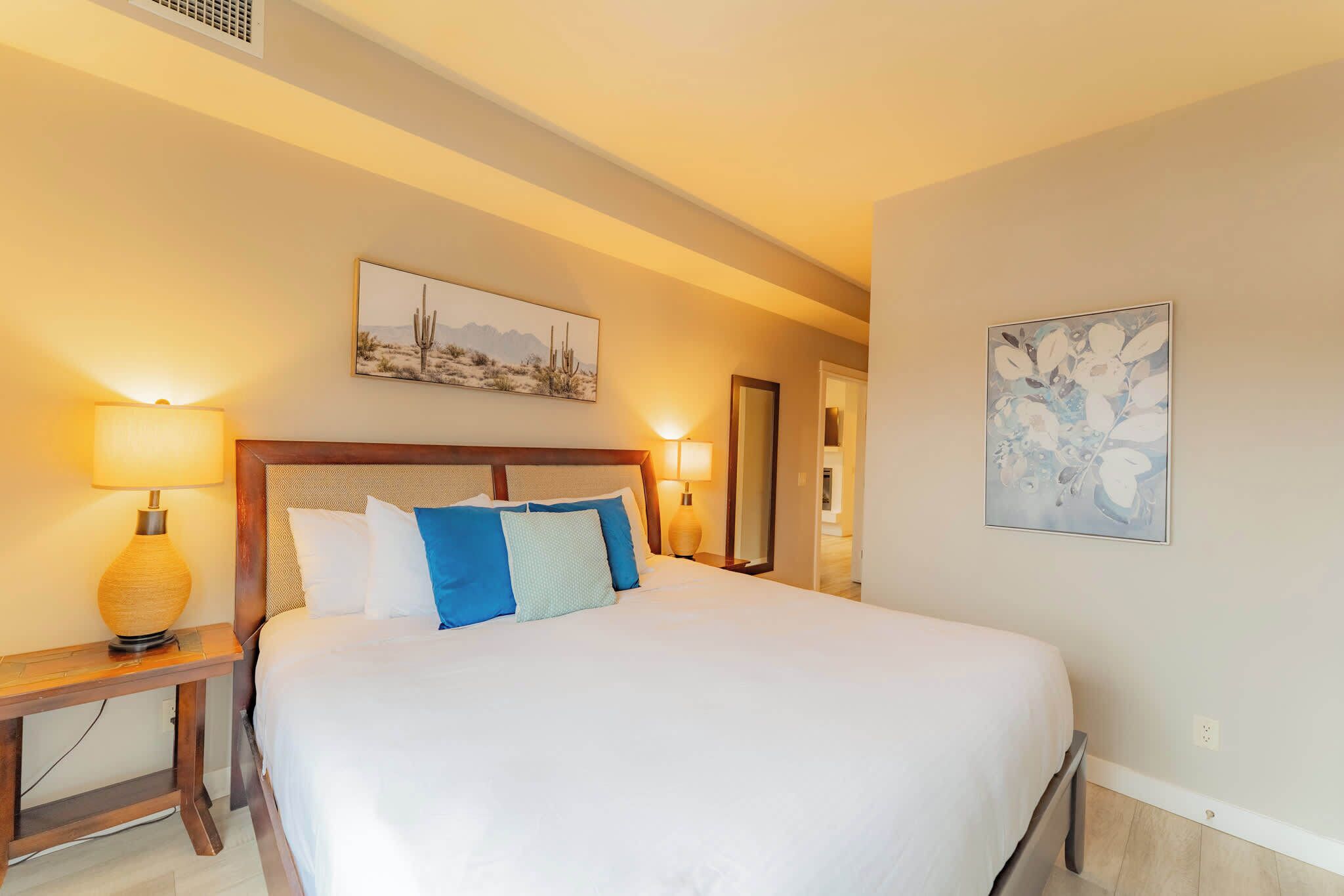 A hotel room with a large bed, two bedside lamps, and two wall-mounted paintings.