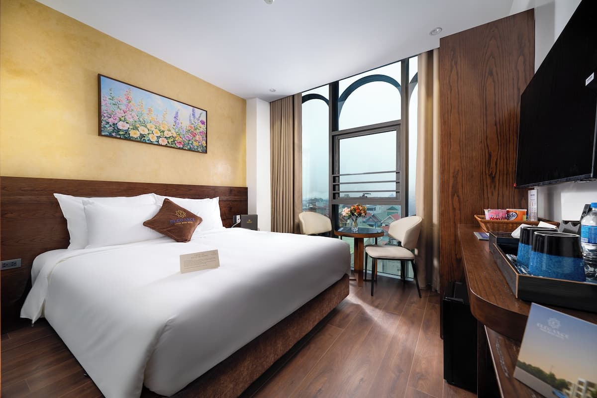 A hotel room with a large bed, a desk with a computer, a chair, and a window with a view.