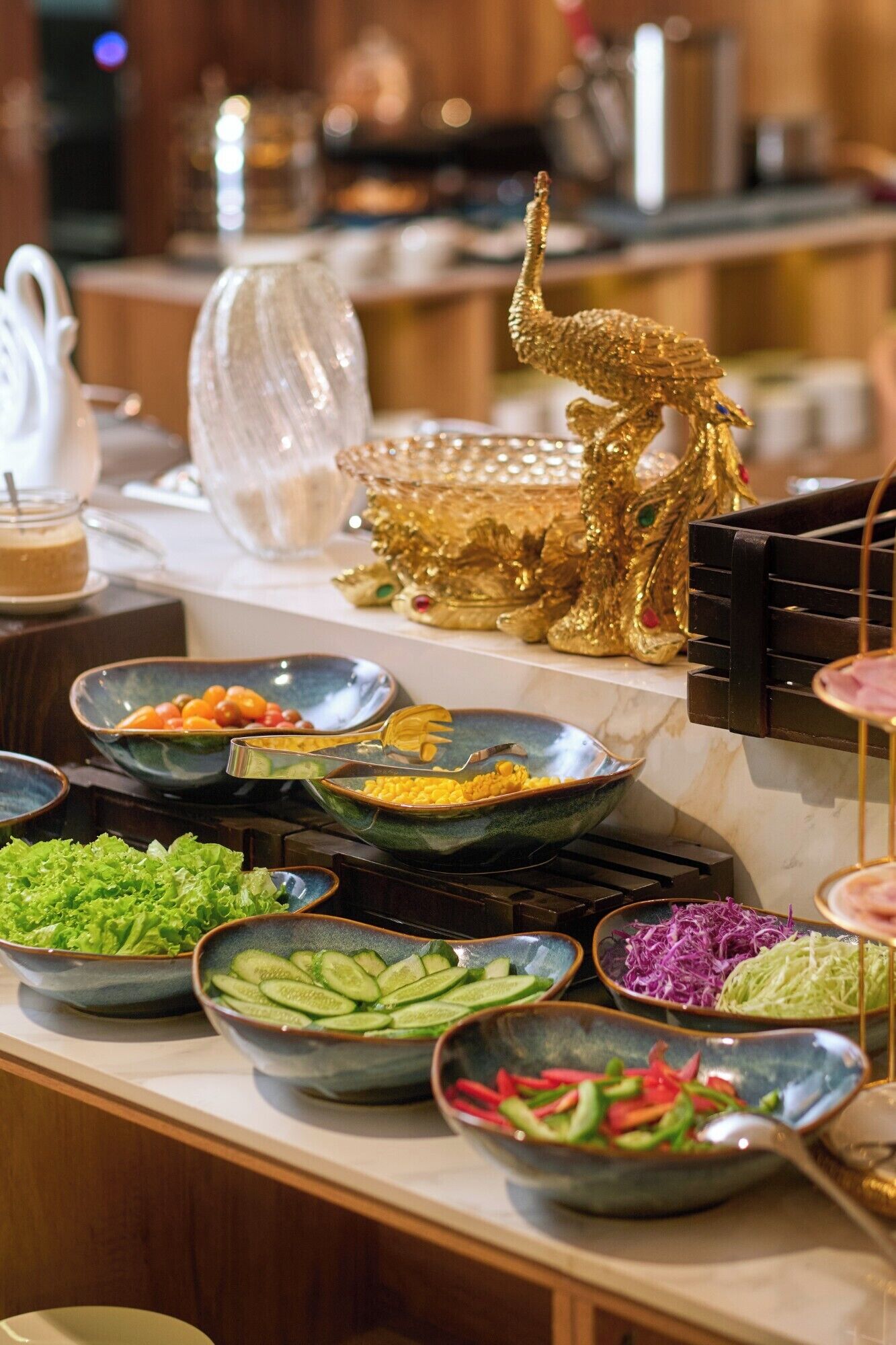 Un buffet proposant une variété de plats, notamment des salades, des légumes et une statue dorée servant d’élément décoratif.