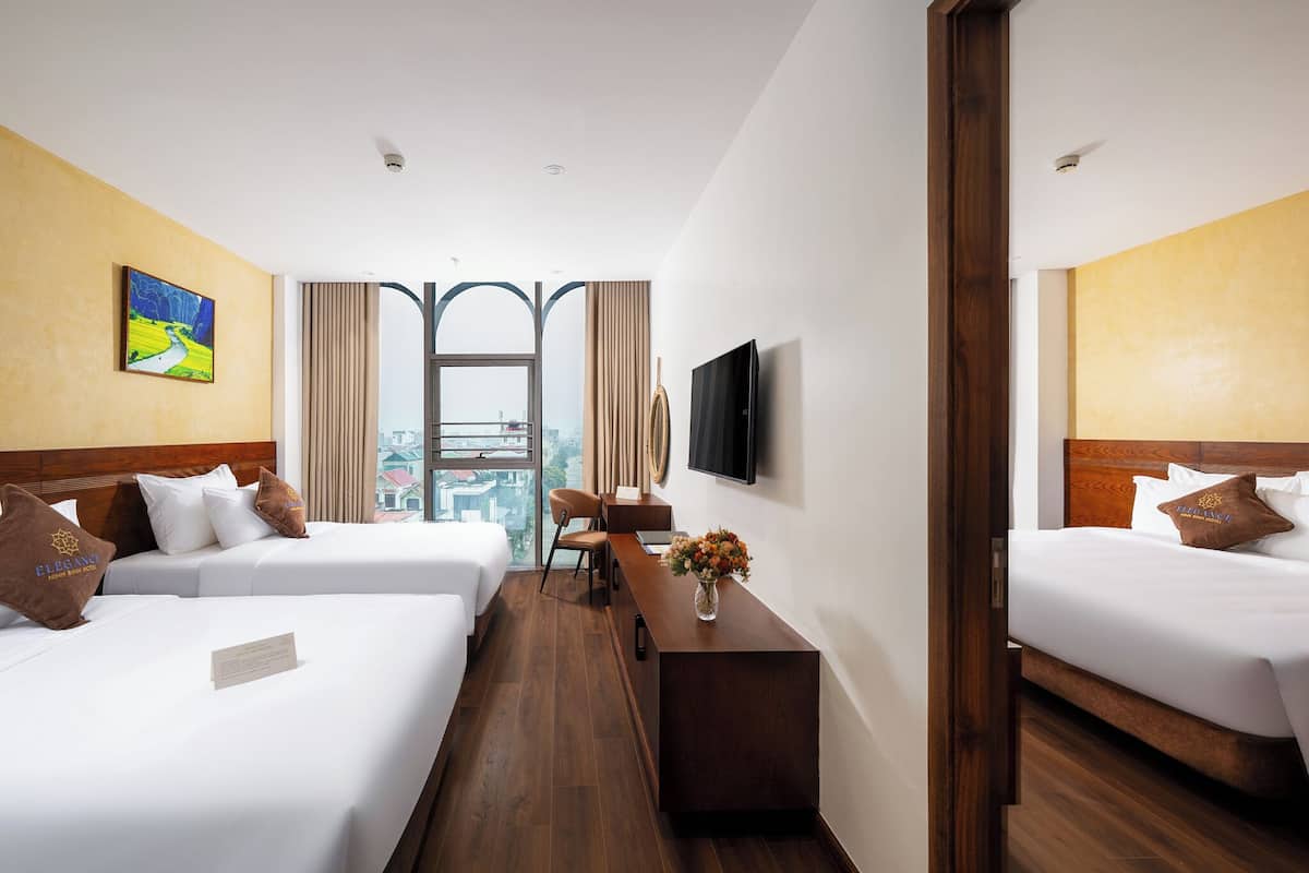 A hotel room with two beds, a desk, a chair, a TV, and a window with a city view.