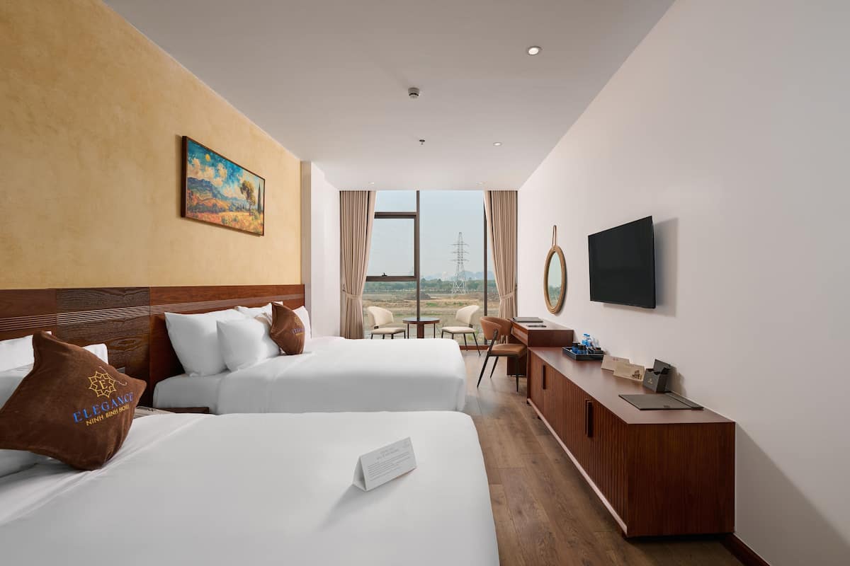A hotel room with two beds, a desk, a TV, and a view of the landscape.