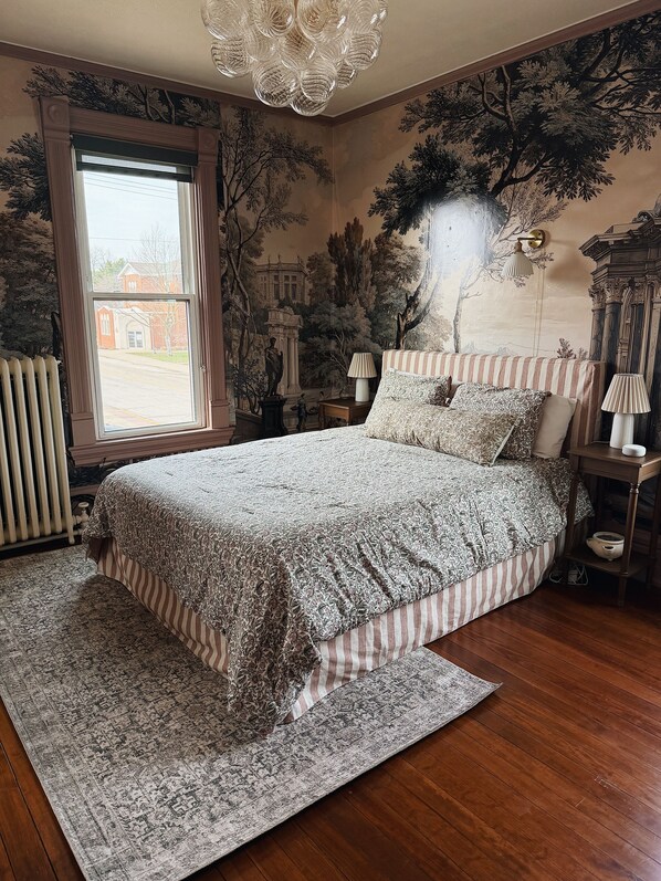 Ein Schlafzimmer mit einem großen Bett, einem Heizkörper, einem Fenster und einem Wandgemälde.