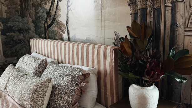 Un dormitorio con cama, ropa de cama a rayas, una lámpara de pared y un jarrón decorativo.