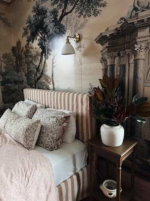 Un dormitorio con cama, ropa de cama a rayas, una lámpara de pared y un jarrón decorativo.