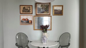 Un comedor con una mesa redonda, dos sillas, un florero con flores y cuadros en la pared.