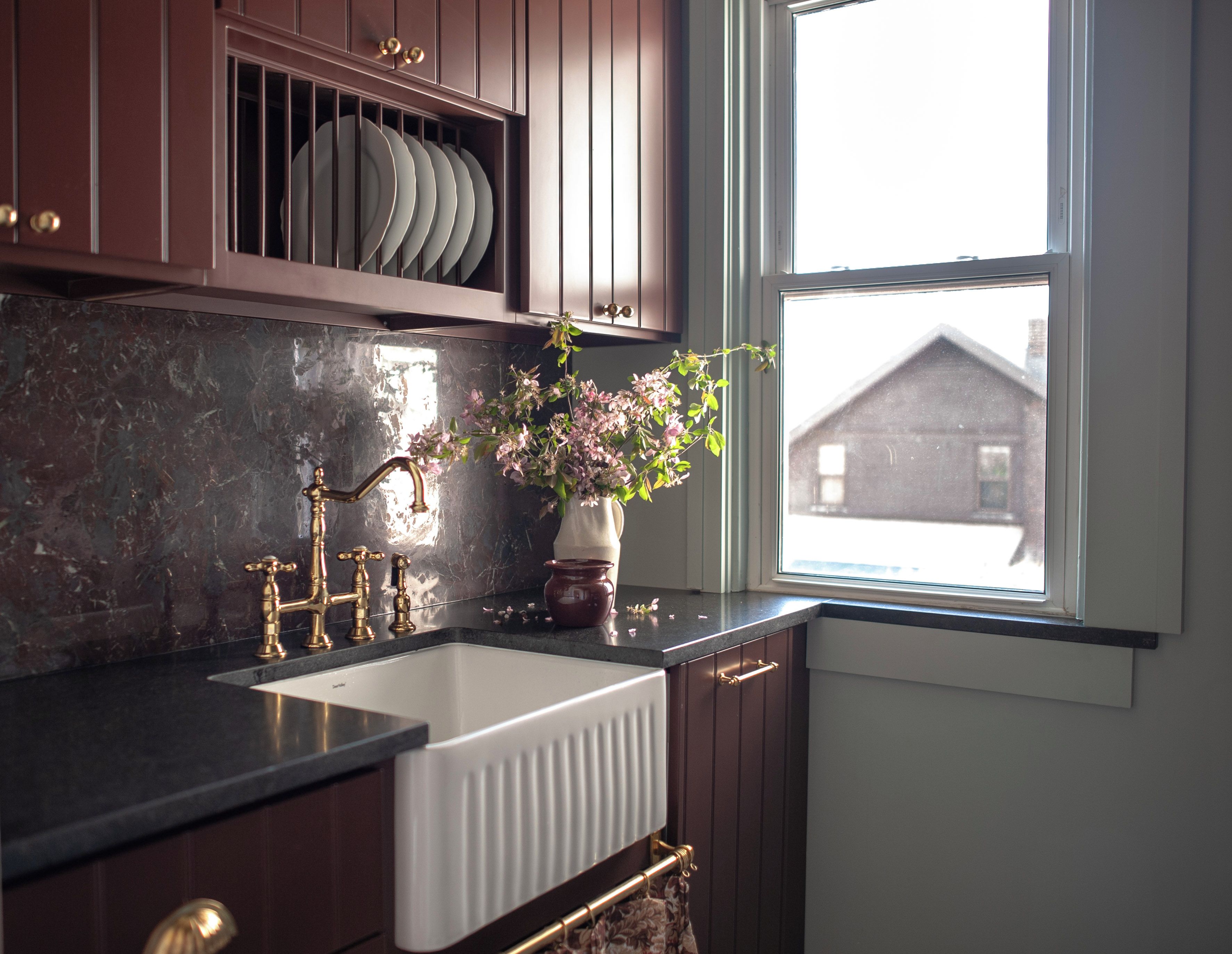 A kitchen with a white sink, dark marble backsplash, and wooden cabinets.