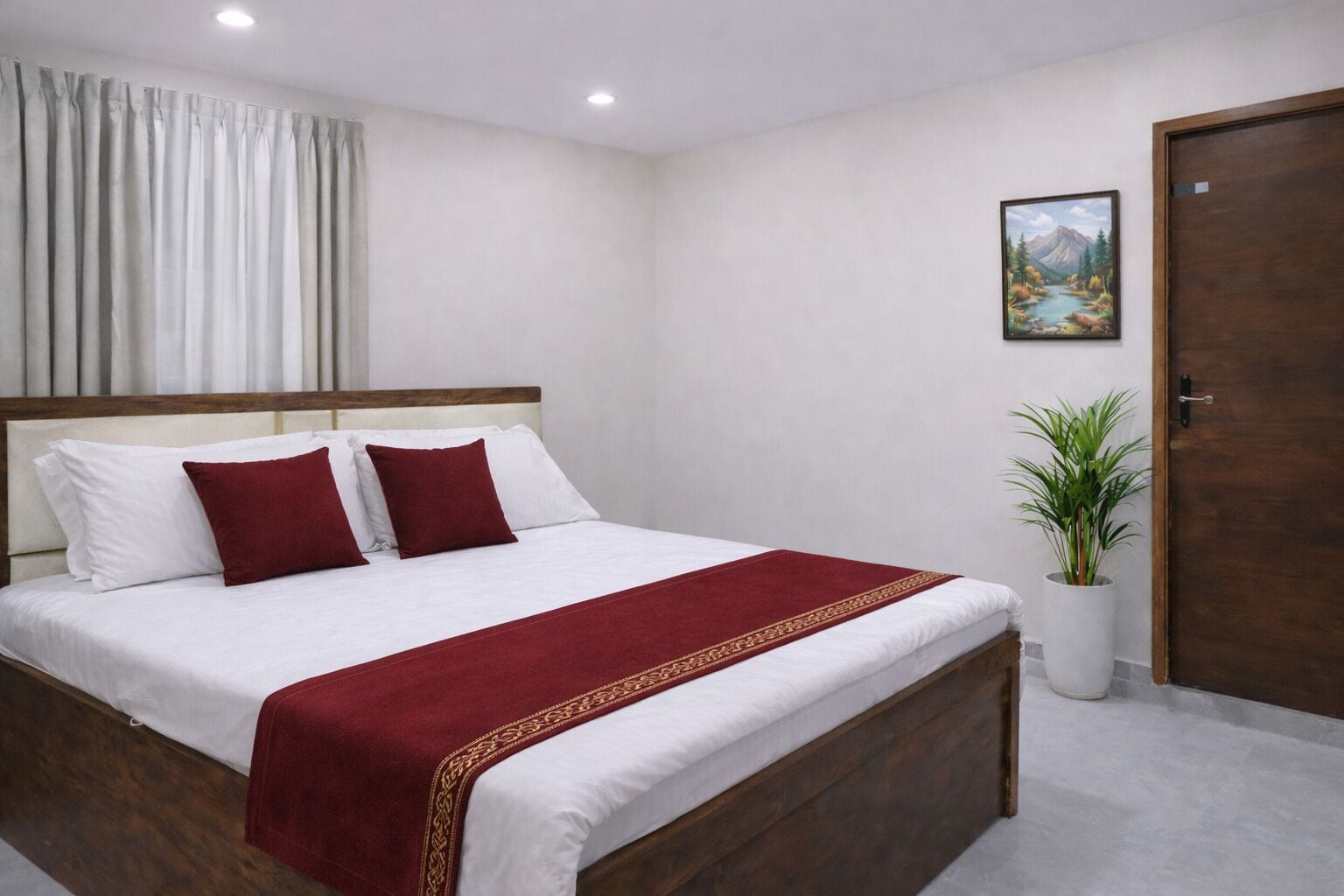 A neatly made bed with white and red bedding, a wooden headboard, a red throw blanket, a potted plant, and a door with a painting above it.
