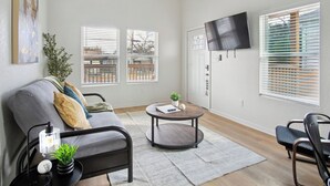 Un salon moderne avec un canapé gris, une table basse ronde et un téléviseur fixé au mur.