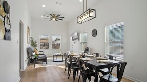 Un espace repas avec une grande table, des chaises noires et un ventilateur de plafond.