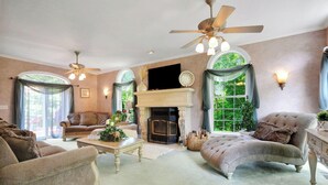 A spacious living room with a fireplace, comfortable seating, and large windows offering a view of greenery. - Spacious 7-bedroom country house in perfect Kingston retreat (Kingston)
