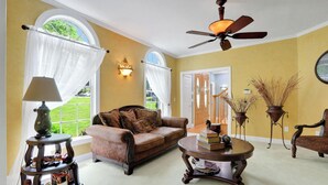 A cozy living room with a brown leather sofa, a round wooden coffee table with books, a floor lamp, and a ceiling fan. - Spacious 7-bedroom country house in perfect Kingston retreat (Kingston)